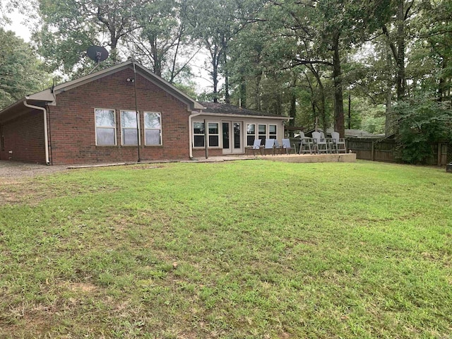 back of house featuring brick siding, a lawn, and fence