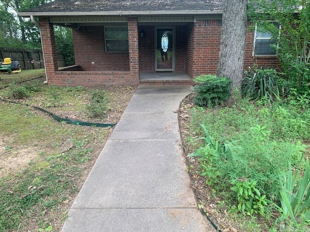 doorway to property with brick siding, a porch, and fence