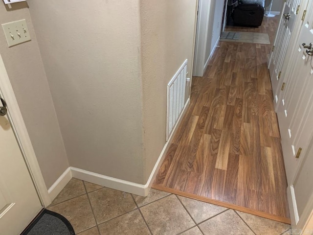 hallway with wood finished floors, visible vents, and baseboards