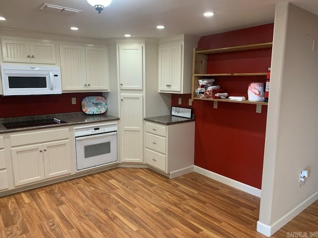 kitchen with white appliances, dark countertops, visible vents, and light wood finished floors