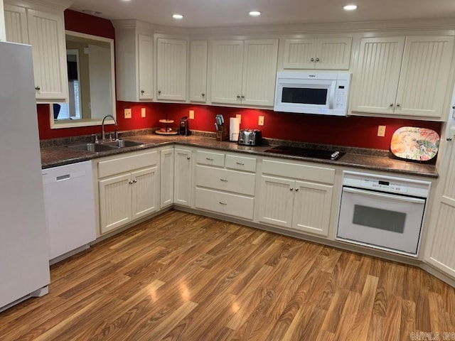 kitchen featuring light wood finished floors, white appliances, dark countertops, and a sink