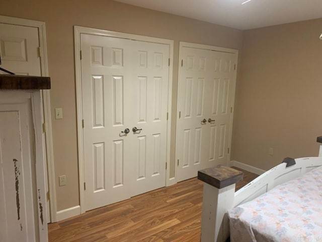 bedroom featuring two closets, baseboards, and wood finished floors