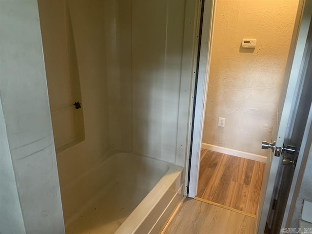 bathroom featuring wood finished floors, baseboards, a textured wall, and a washtub