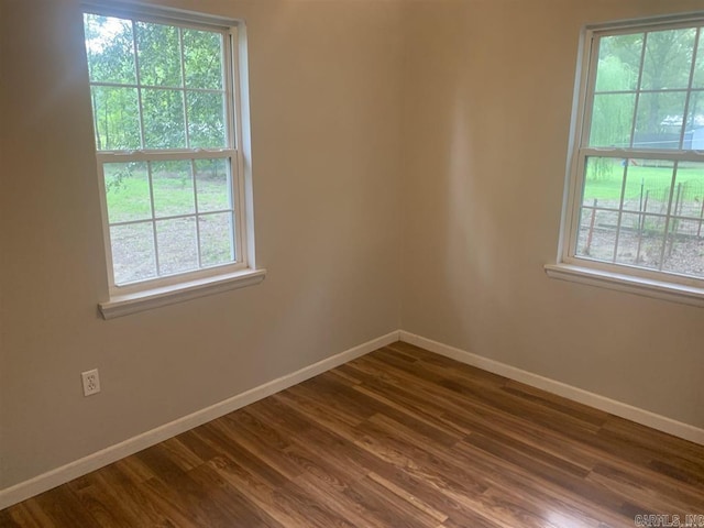 empty room with a healthy amount of sunlight, dark wood-type flooring, and baseboards