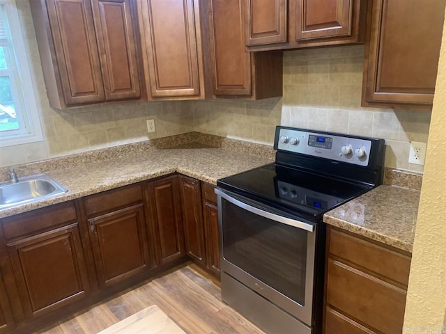 kitchen featuring a sink, light wood-type flooring, tasteful backsplash, and stainless steel range with electric cooktop