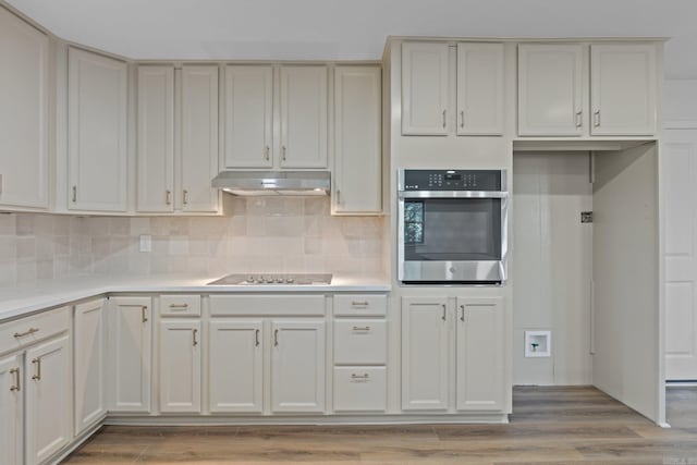 kitchen featuring tasteful backsplash, oven, under cabinet range hood, light countertops, and black electric cooktop