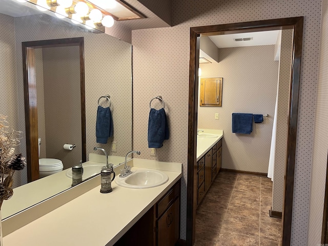 bathroom with toilet, two vanities, visible vents, and a sink