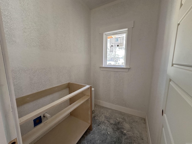 interior space featuring baseboards, unfinished concrete flooring, and a textured wall