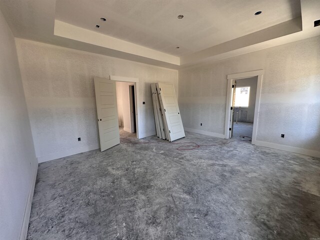 unfurnished bedroom featuring a tray ceiling, baseboards, and a textured wall