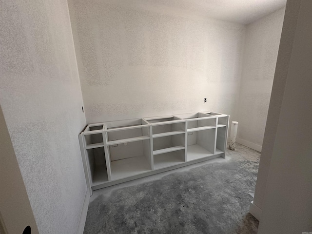 interior space with unfinished concrete flooring and a textured wall