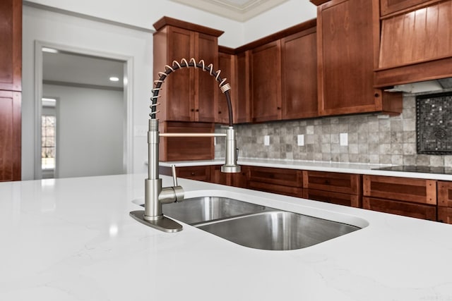 kitchen with a sink, black electric stovetop, tasteful backsplash, and light stone counters