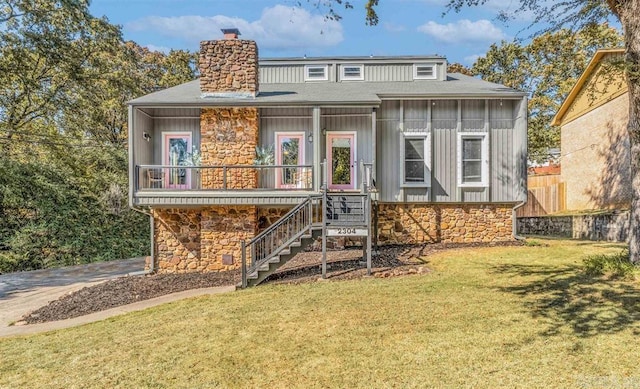 rear view of house featuring a porch, a yard, a chimney, stairs, and stone siding