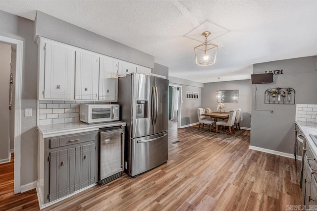 kitchen featuring light wood-type flooring, backsplash, wine cooler, stainless steel fridge, and white cabinets