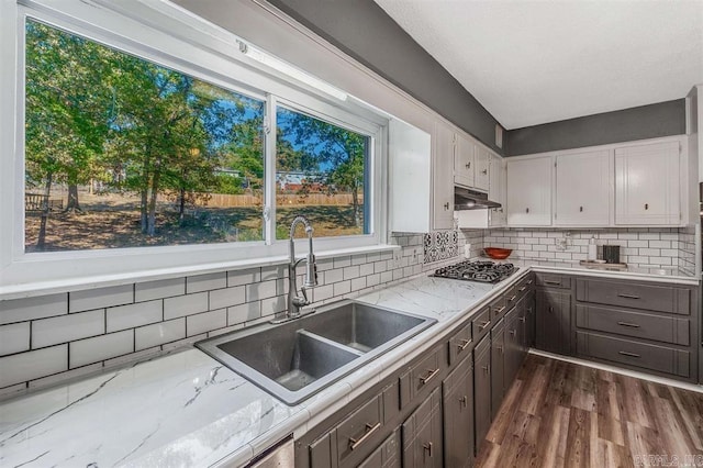 kitchen featuring a sink, tasteful backsplash, dark wood-style floors, white cabinets, and stainless steel gas cooktop