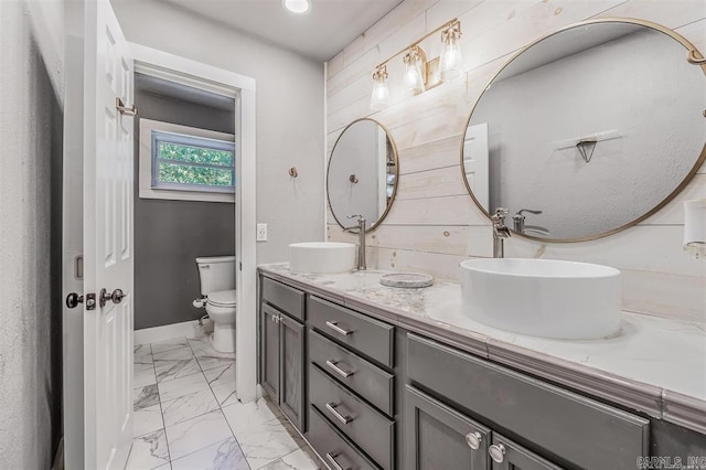 bathroom featuring double vanity, toilet, marble finish floor, and a sink