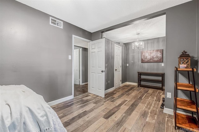 bedroom with visible vents, a textured ceiling, baseboards, and wood finished floors