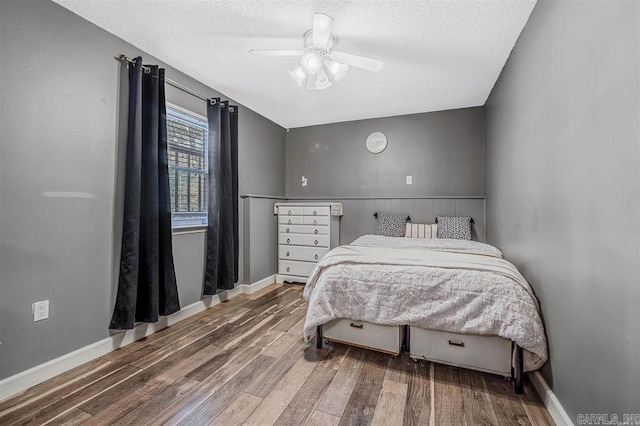 bedroom featuring a wainscoted wall, a textured ceiling, a ceiling fan, and wood finished floors