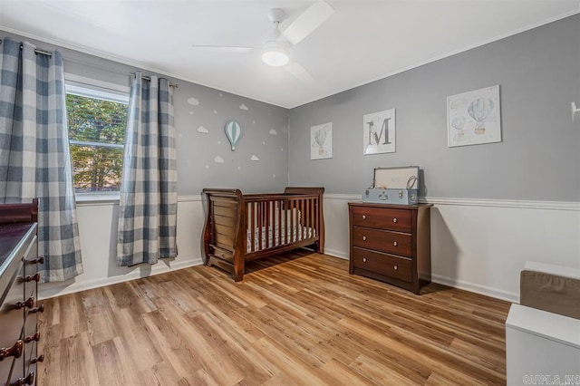 bedroom featuring a crib, ornamental molding, wood finished floors, baseboards, and ceiling fan