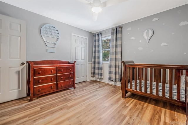 bedroom with ceiling fan, a nursery area, and wood finished floors