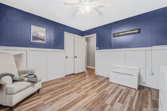 living area with a ceiling fan, visible vents, wood finished floors, and a wainscoted wall