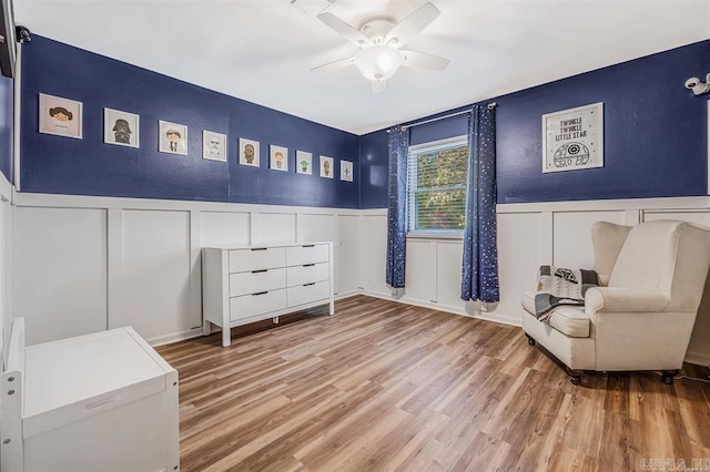 sitting room with a wainscoted wall, a decorative wall, a ceiling fan, and wood finished floors