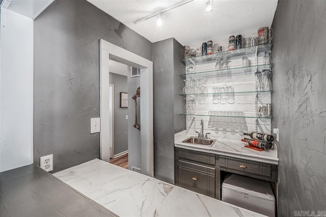 bar with indoor wet bar, a textured ceiling, rail lighting, and a sink