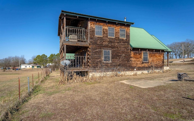 back of property featuring a balcony, fence, and metal roof