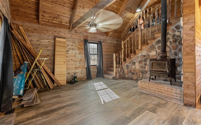 unfurnished living room with wooden walls, wood finished floors, lofted ceiling with beams, a wood stove, and wood ceiling