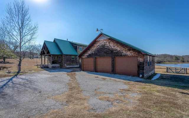 view of side of home featuring a detached garage, fence, a water view, log siding, and metal roof