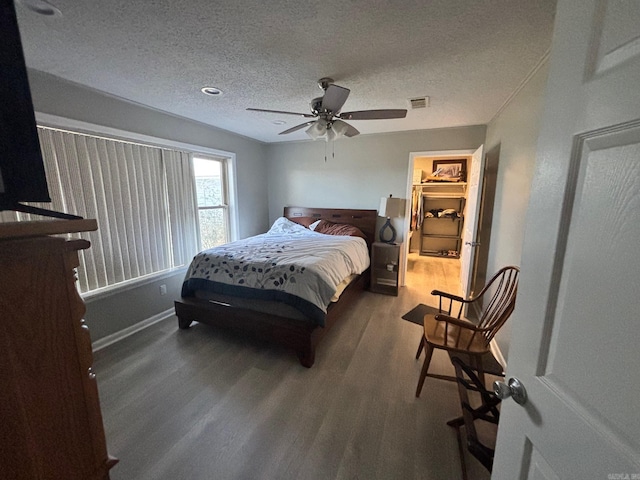 bedroom featuring visible vents, a textured ceiling, wood finished floors, ceiling fan, and a spacious closet