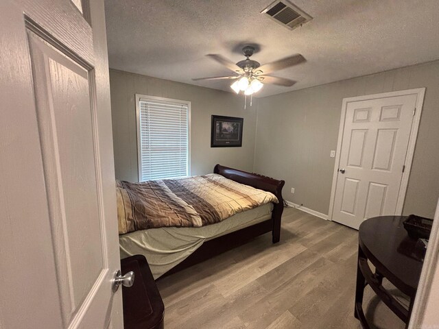 bedroom with visible vents, baseboards, wood finished floors, a textured ceiling, and a ceiling fan