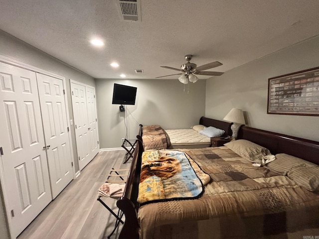 bedroom featuring visible vents, multiple closets, light wood-style floors, and a textured ceiling