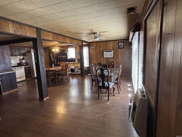 dining area featuring wooden walls, dark wood-style floors, visible vents, ceiling fan, and a wall mounted air conditioner