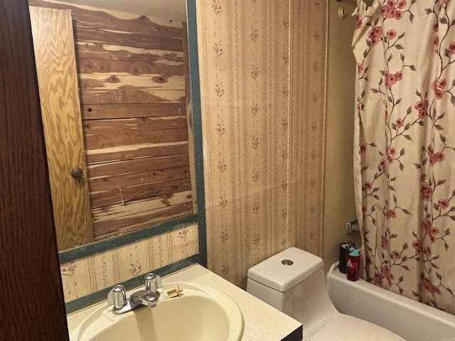 full bath with toilet, shower / bath combo, vanity, and wallpapered walls