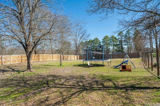 view of yard featuring a trampoline, a fenced backyard, and a playground