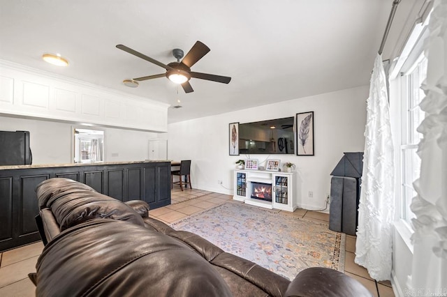 living room featuring a glass covered fireplace, light tile patterned floors, and ceiling fan