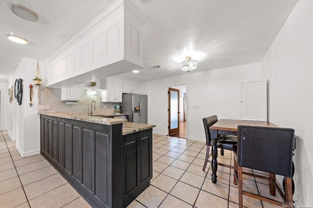 kitchen with backsplash, white cabinets, a peninsula, light tile patterned flooring, and stainless steel fridge