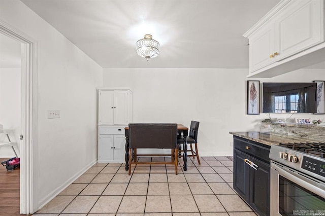 kitchen with light stone countertops, baseboards, light tile patterned flooring, stainless steel range with gas stovetop, and white cabinetry