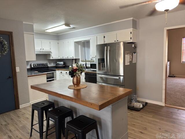 kitchen featuring under cabinet range hood, light wood-type flooring, appliances with stainless steel finishes, and white cabinetry