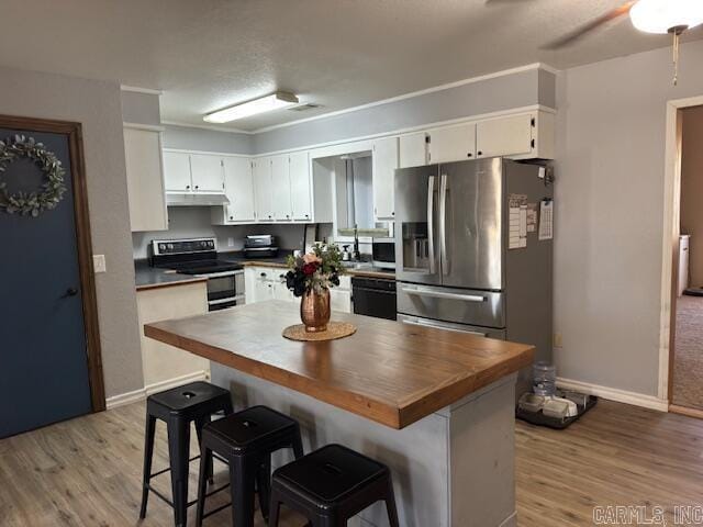 kitchen featuring white cabinetry, under cabinet range hood, light wood-type flooring, and appliances with stainless steel finishes