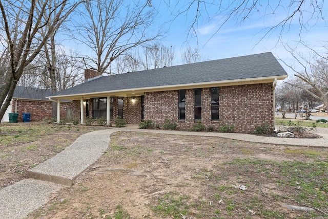 view of front facade with brick siding, a chimney, and a shingled roof