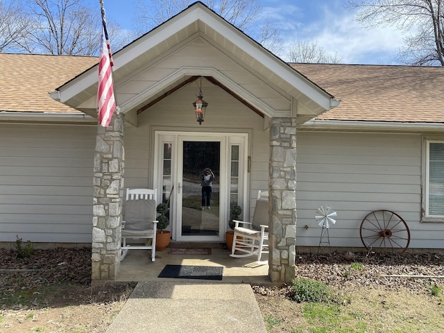 view of exterior entry with roof with shingles