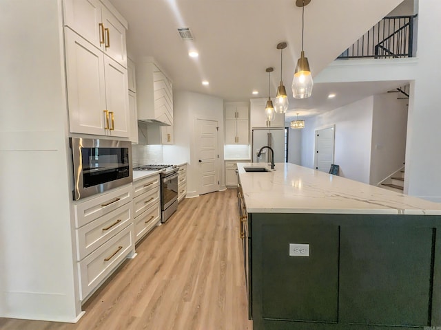 kitchen featuring built in appliances, light wood-style floors, a large island, white cabinets, and a sink