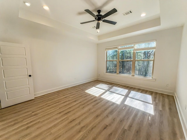 unfurnished room with visible vents, a raised ceiling, baseboards, and wood finished floors