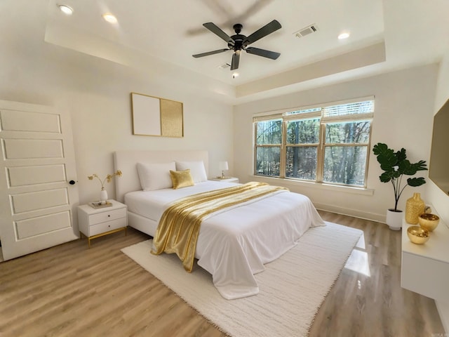 bedroom featuring a tray ceiling, visible vents, and light wood finished floors