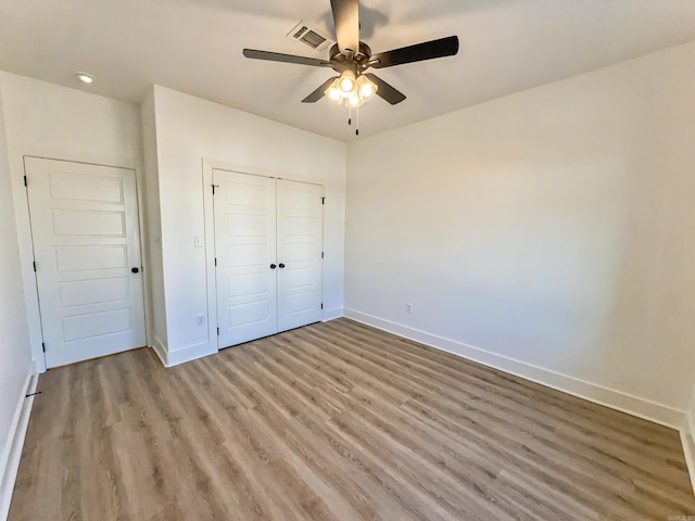 unfurnished bedroom featuring visible vents, baseboards, a closet, and wood finished floors