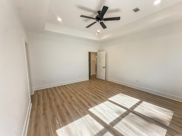 spare room with visible vents, a raised ceiling, wood finished floors, recessed lighting, and baseboards