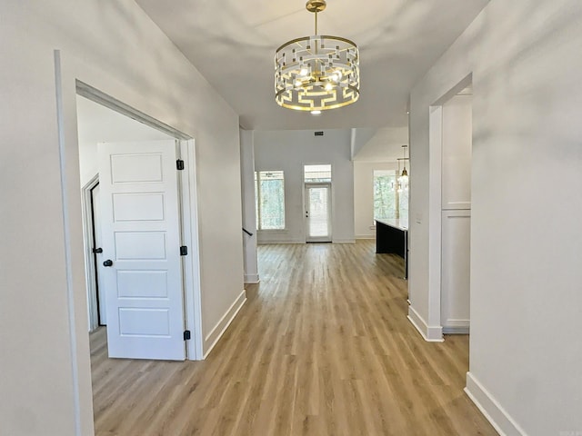 hall featuring a chandelier, baseboards, and light wood-style flooring