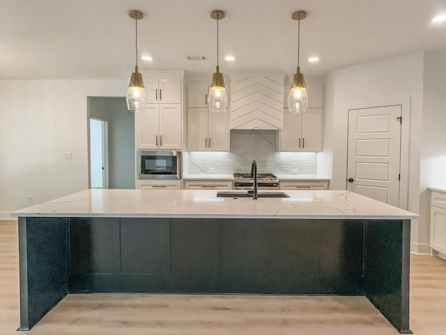 kitchen featuring custom exhaust hood, a sink, a large island, light wood-style floors, and stainless steel microwave