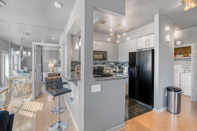 kitchen featuring washing machine and clothes dryer, a notable chandelier, range with electric stovetop, and black refrigerator with ice dispenser